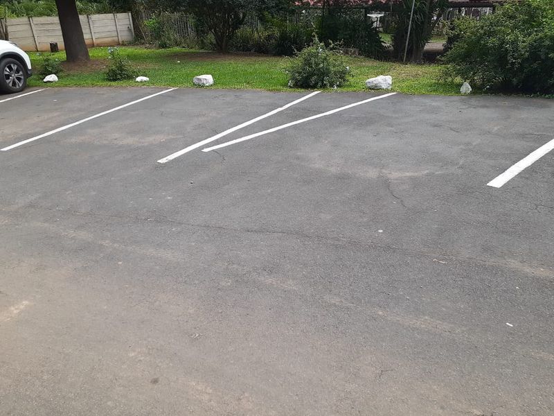An outdoor asphalt parking area with marked bays and a boundary wall in the background.