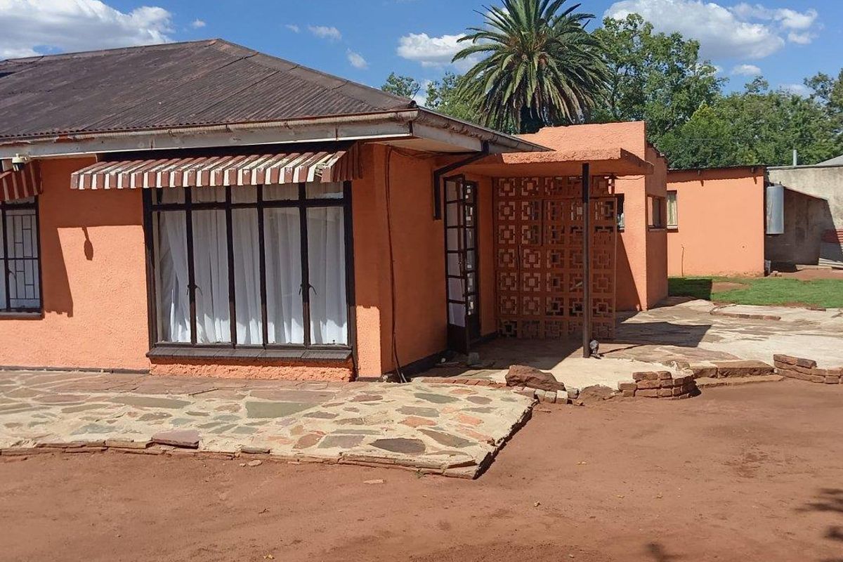 Rear view of the house featuring a stone paved patio, breeze block architectural detail, and corrugated metal roofing with an attached window awning.