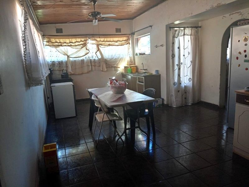 A functional kitchen area featuring tiled flooring, a timber ceiling, and a built-in sink, currently requiring cosmetic updates to the wall finishes.