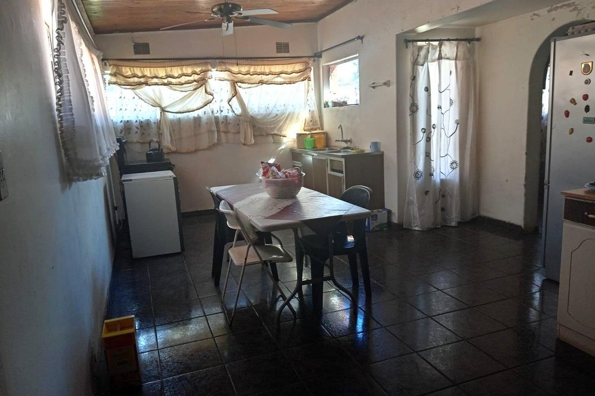 A functional kitchen area featuring tiled flooring, a timber ceiling, and a built-in sink, currently requiring cosmetic updates to the wall finishes.