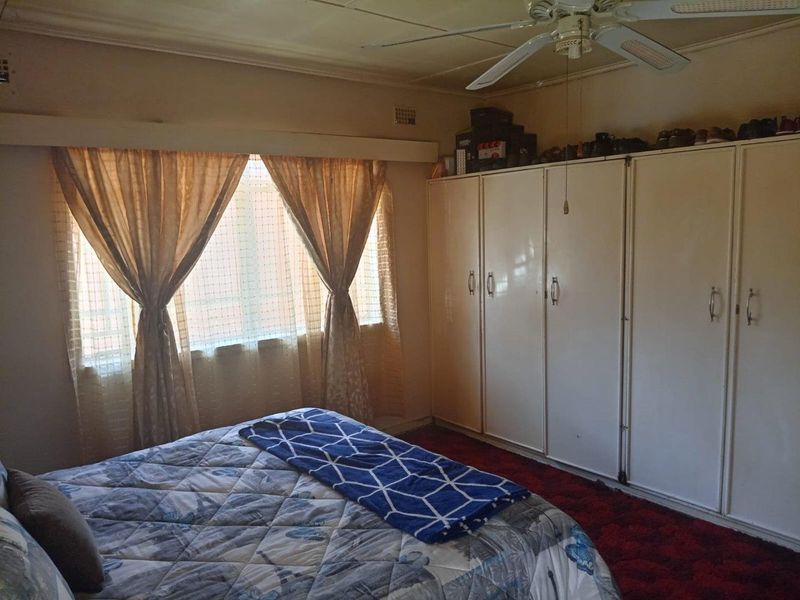 A bedroom featuring built-in cupboards and a ceiling fan, with carpeted flooring and natural light from the window.