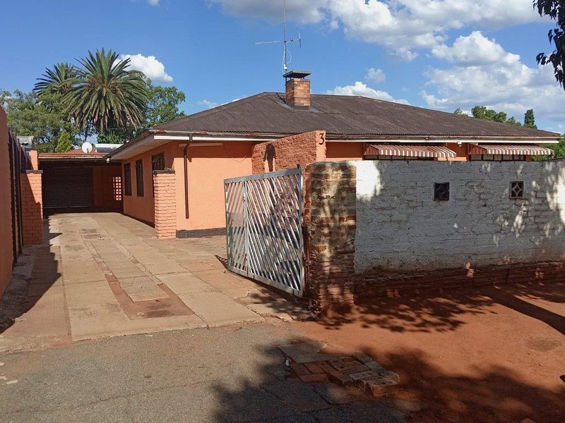 Front exterior view of a single-story house featuring a brick facade, concrete driveway, and a gated entrance with a perimeter boundary wall.