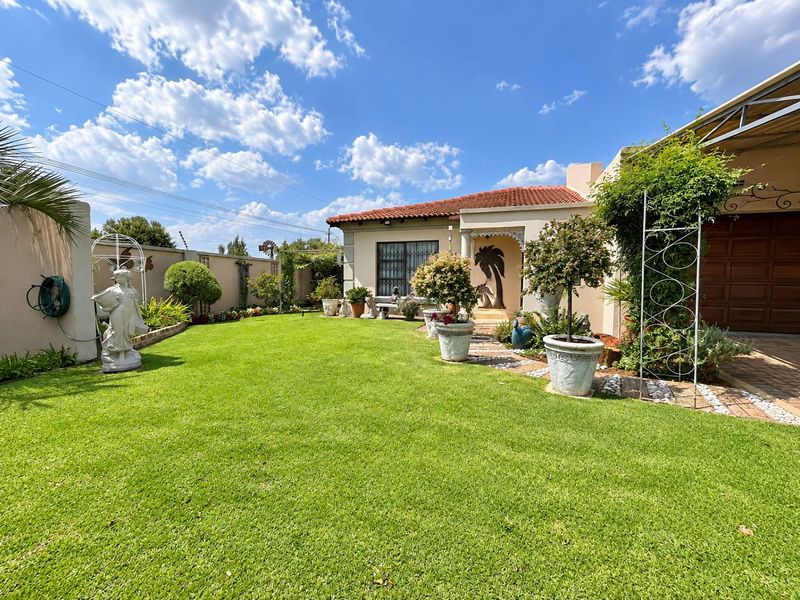 A well-maintained front garden and facade of a townhouse, featuring a manicured lawn, paved pathway, and secure garage access.