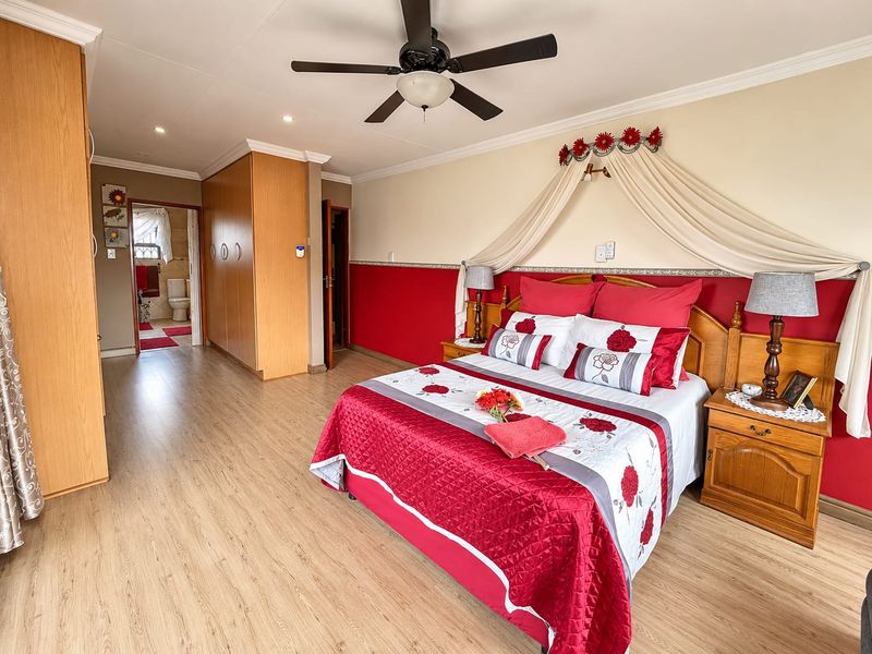 Spacious bedroom featuring laminate flooring, built-in wooden cupboards, a ceiling fan, and direct access to an en-suite bathroom.