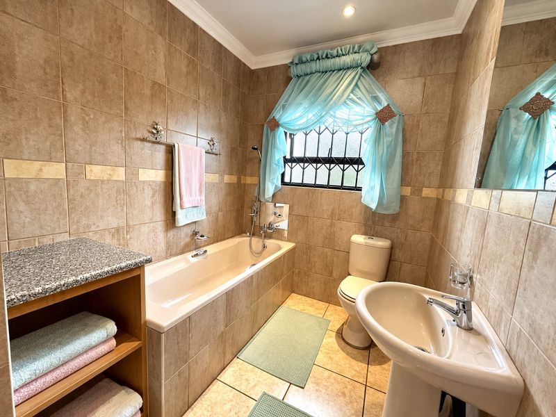A functional bathroom featuring a bathtub, pedestal sink, toilet, and neutral floor-to-ceiling wall tiles with a built-in vanity counter.