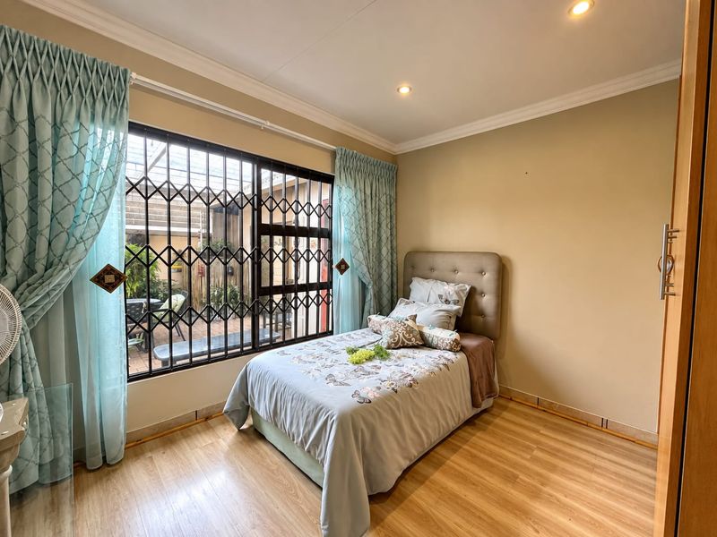 A bedroom featuring laminate flooring, recessed downlights, and a built-in cupboard, with a security gate over the window overlooking the rear patio.