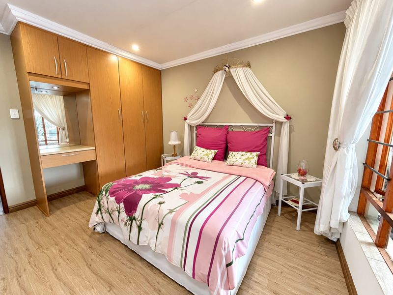 A well-maintained bedroom featuring light wood-look laminate flooring, built-in cabinetry with an integrated vanity, and recessed ceiling lighting.