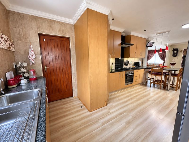 Open-plan kitchen and dining area featuring light wood-look laminate flooring, granite countertops, built-in cabinetry, and a functional layout with integrated oven and extractor fan.