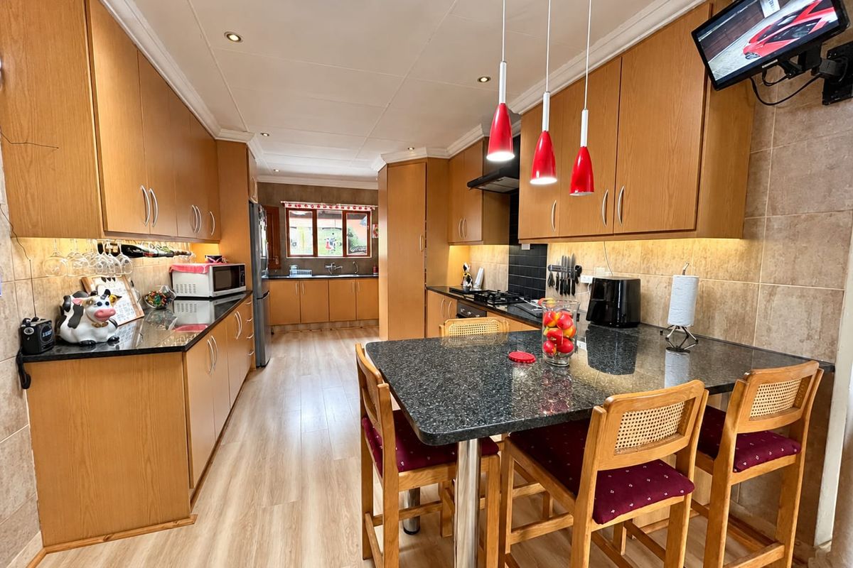 Spacious kitchen featuring wood-finish cabinetry, granite countertops, a central breakfast bar, and integrated lighting, offering a functional and well-maintained cooking and dining space.