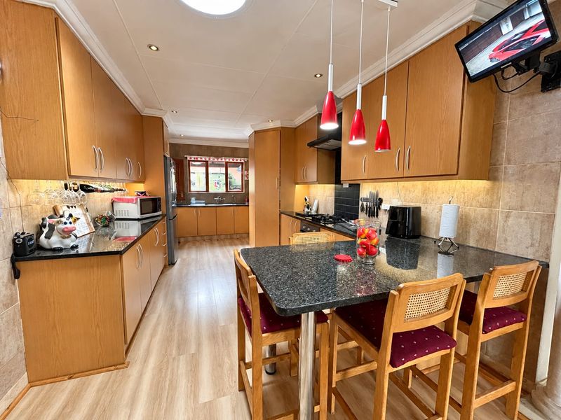 Spacious kitchen featuring wood-finish cabinetry, granite countertops, a central breakfast bar, and integrated lighting, offering a functional and well-maintained cooking and dining space.