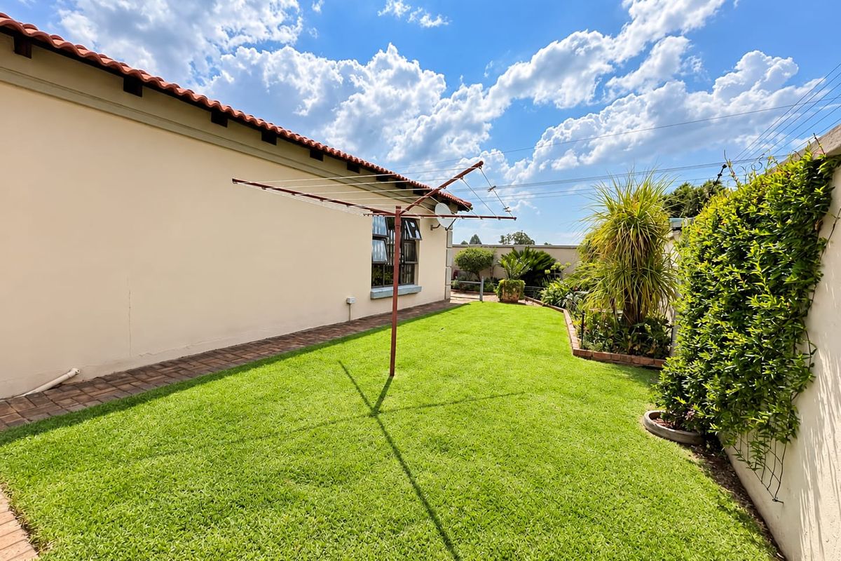 A well-maintained rear garden featuring a lush lawn, paved pathway, and a rotary clothesline, enclosed by a secure boundary wall.