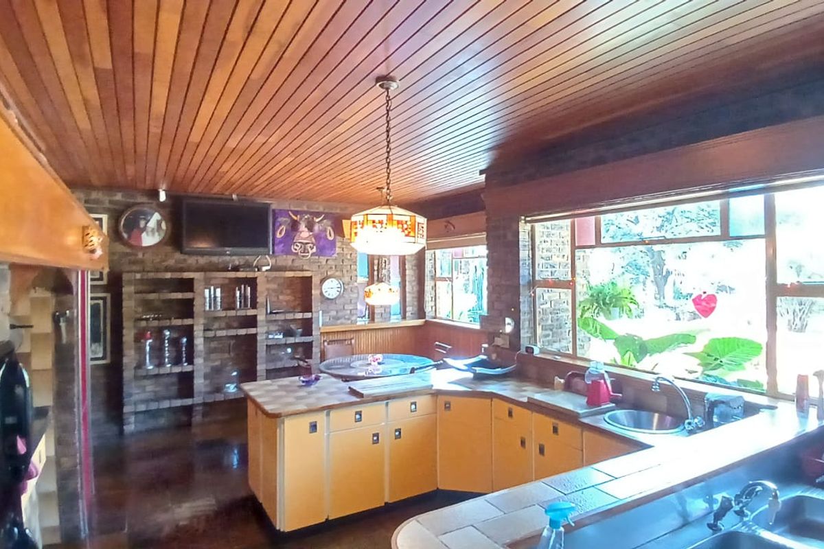 Spacious kitchen featuring exposed brick walls, a timber-clad ceiling, and large windows, offering a rustic aesthetic with ample counter space and built-in storage.