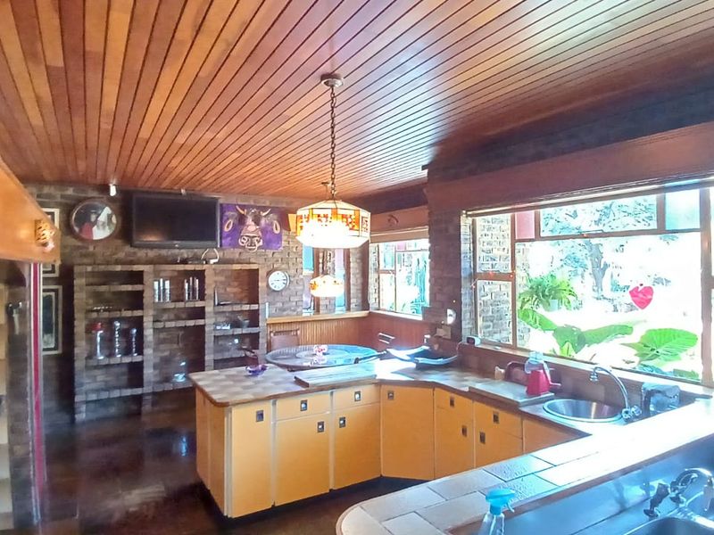 Spacious kitchen featuring exposed brick walls, a timber-clad ceiling, and large windows, offering a rustic aesthetic with ample counter space and built-in storage.