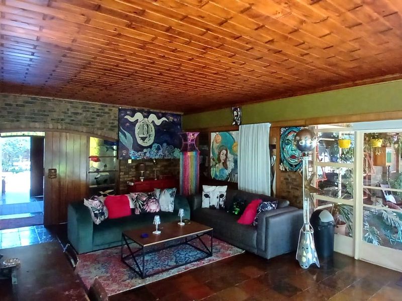 Spacious living room featuring a warm timber tongue and groove ceiling, exposed brick accents, and tiled flooring with direct access to an outdoor patio area.