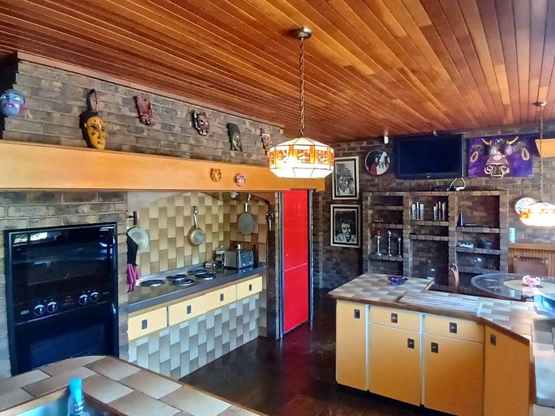 Spacious kitchen featuring a timber ceiling, brick feature walls, built-in oven, electric hob, and tiled countertops with ample built-in cabinetry.