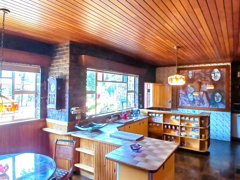 Open plan kitchen and dining area featuring a timber ceiling, exposed brickwork, and extensive built-in wooden cabinetry with tiled countertops.