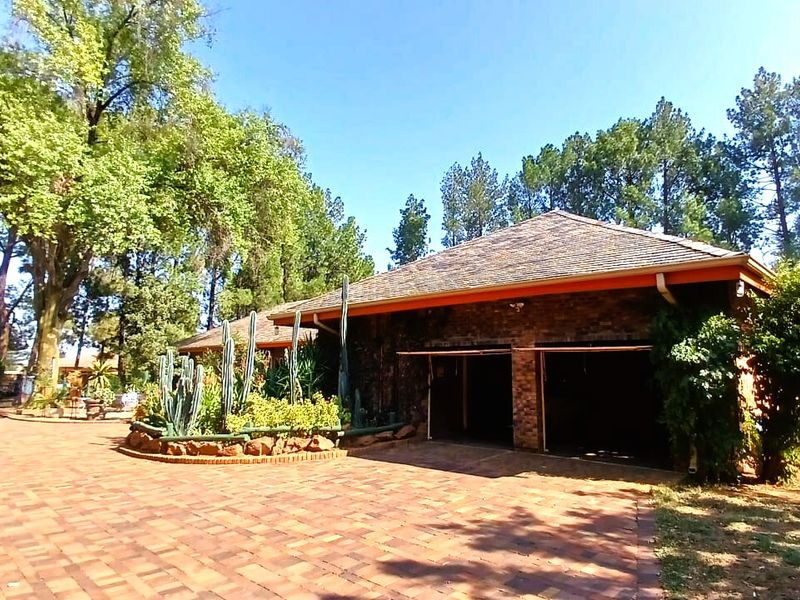 Front view of a brick-faced house featuring a double garage and a paved driveway surrounded by mature trees and landscaped garden beds.