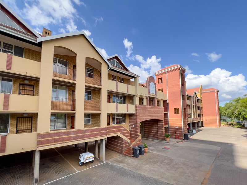Exterior view of a multi-story apartment complex featuring brick facade, covered parking bays, and private balconies.