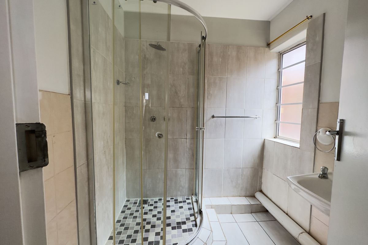 A functional bathroom featuring a curved glass shower enclosure, wall-mounted basin, and neutral tiled finishes, offering potential for modernization.