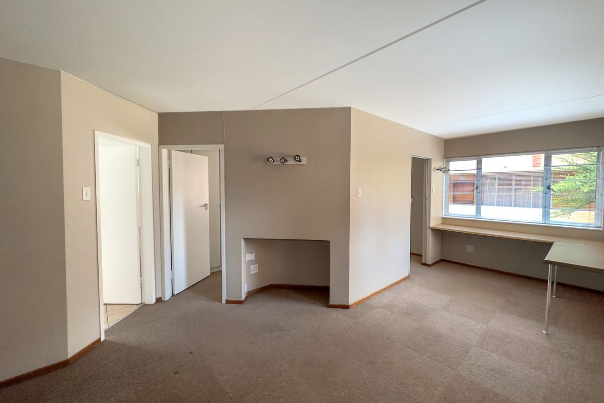 An empty living area featuring neutral walls, carpeted flooring, a built-in desk space under the window, and a recessed wall niche.