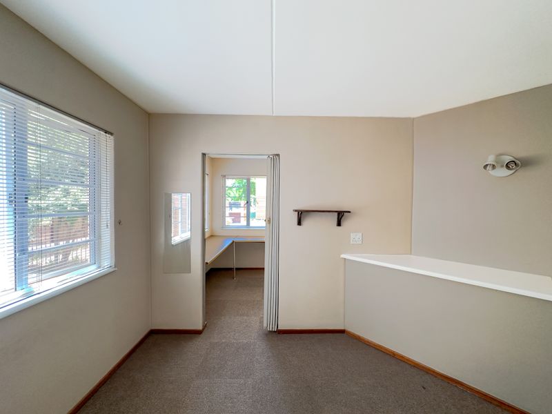 An empty bedroom featuring neutral walls, carpet flooring, a folding door leading to an adjacent space, and a built-in ledge with wall-mounted lighting.