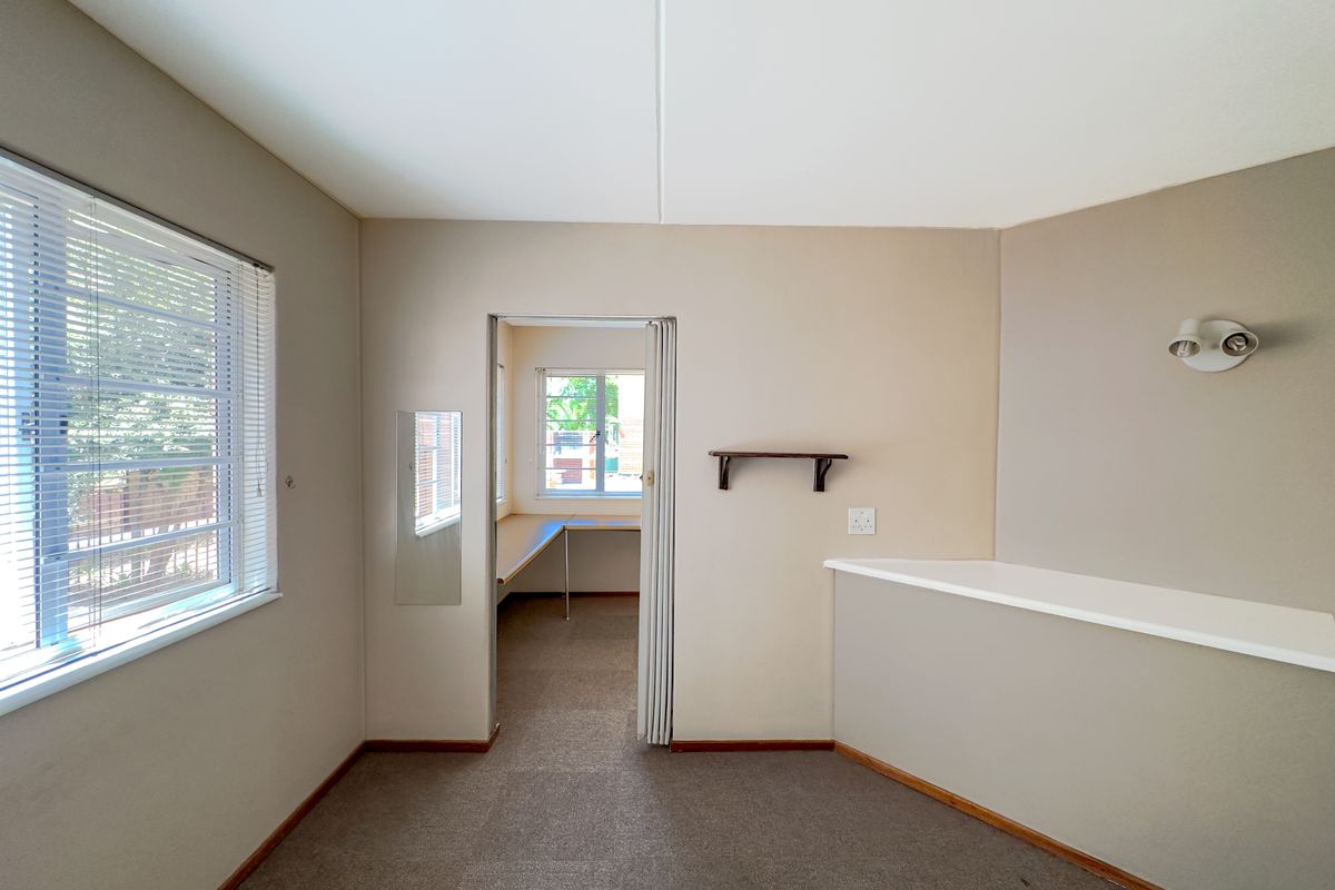 An empty bedroom featuring neutral walls, carpet flooring, a folding door leading to an adjacent space, and a built-in ledge with wall-mounted lighting.