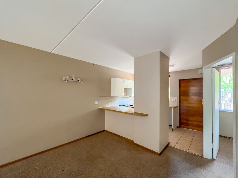 An open-plan living and kitchen area featuring a breakfast bar, neutral wall tones, and a mix of carpeted and tiled flooring.
