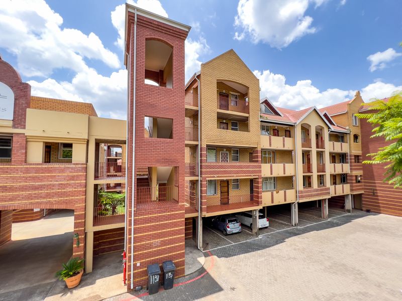 Exterior view of a multi-story apartment complex featuring brick facade architecture, integrated stairwell towers, and covered ground-level parking bays.