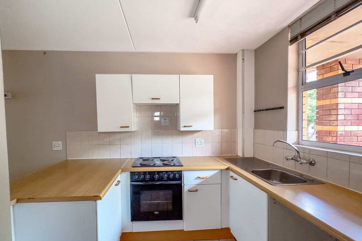 A functional kitchen featuring white cabinetry, laminate countertops, a built-in oven and hob, and a stainless steel sink with tiled backsplash.