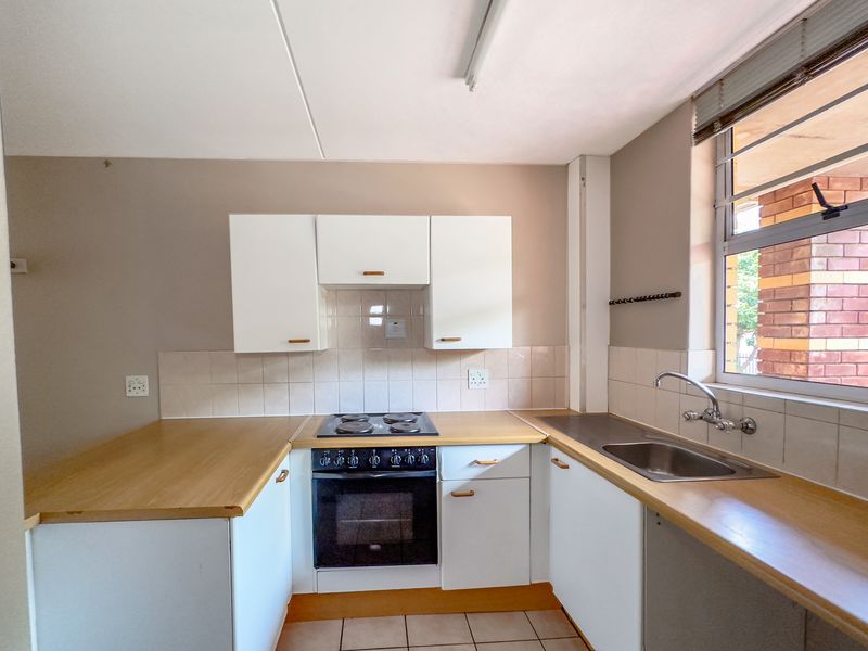 A functional kitchen featuring white cabinetry, laminate countertops, a built-in oven and hob, and a stainless steel sink with tiled backsplash.