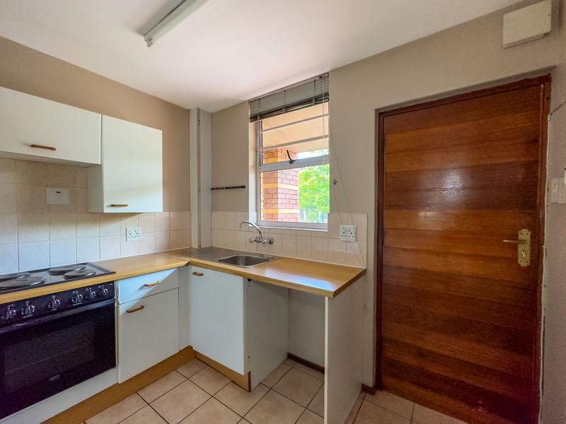 A functional kitchen featuring built-in cabinetry, laminate countertops, a stainless steel sink, and an integrated electric stove with tiled backsplash and flooring.