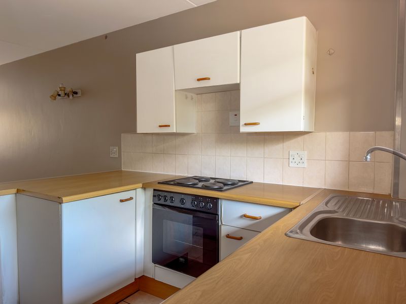 A functional kitchen featuring white cabinetry, laminate countertops, a built-in oven with electric hob, and a stainless steel sink with tiled backsplash.