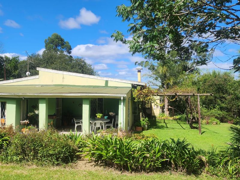 Rear view of the farmhouse featuring a covered patio, established garden, and a timber pergola set within a lush, green landscape.