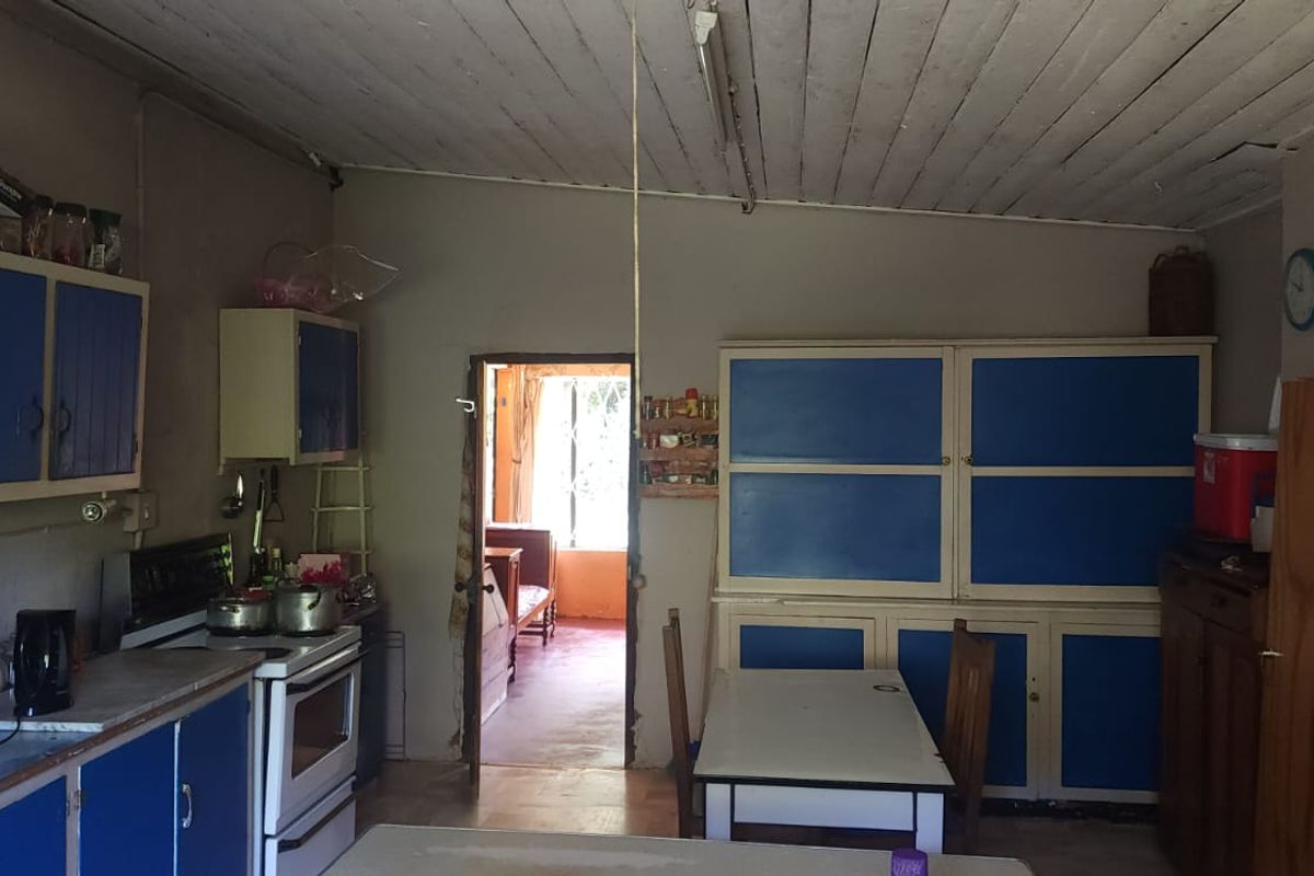 A dated kitchen featuring blue cabinetry, a freestanding stove, and a timber ceiling, offering potential for modernization and renovation.