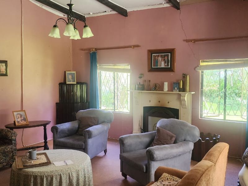 A living room featuring a traditional fireplace with mantelpiece, exposed ceiling beams, and security bars on the windows, requiring cosmetic updates.