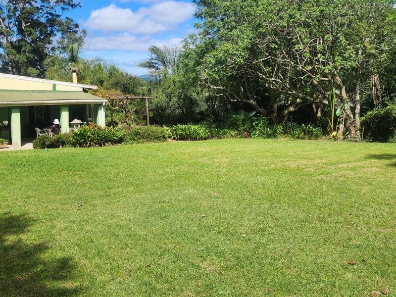 A spacious rear garden featuring a well-maintained lawn, mature trees, and a covered patio area attached to the main farmhouse structure.