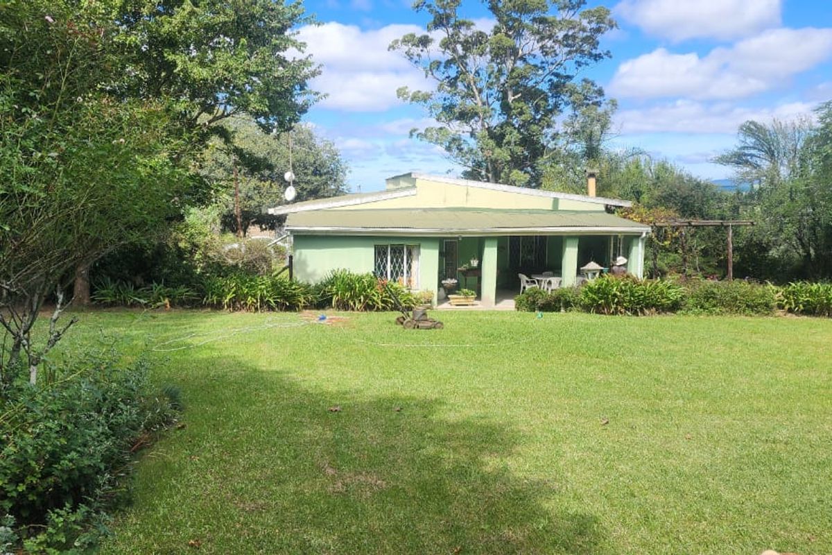 A rear view of the farmhouse featuring a covered patio area overlooking a spacious, well-maintained green lawn and mature garden surroundings.