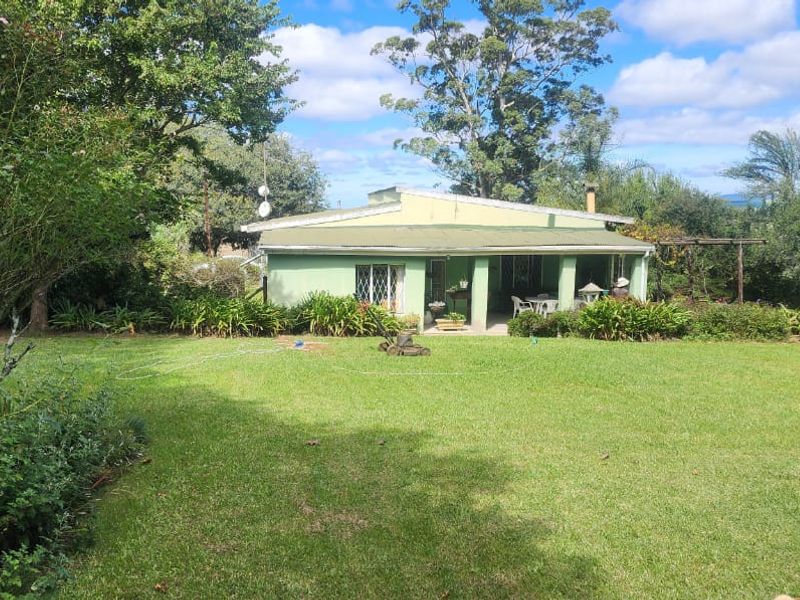 A rear view of the farmhouse featuring a covered patio area overlooking a spacious, well-maintained green lawn and mature garden surroundings.