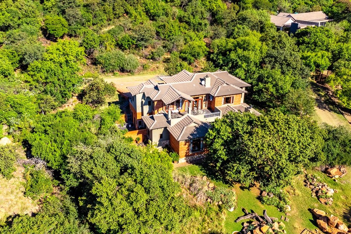 Aerial view of a large residential property nestled within a lush, wooded landscape, featuring a multi-pitched tiled roof and expansive outdoor garden areas.