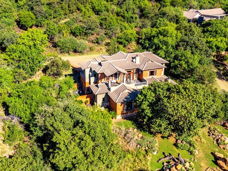 Aerial view of a large residential property nestled within a lush, wooded landscape, featuring a multi-pitched tiled roof and expansive outdoor garden areas.