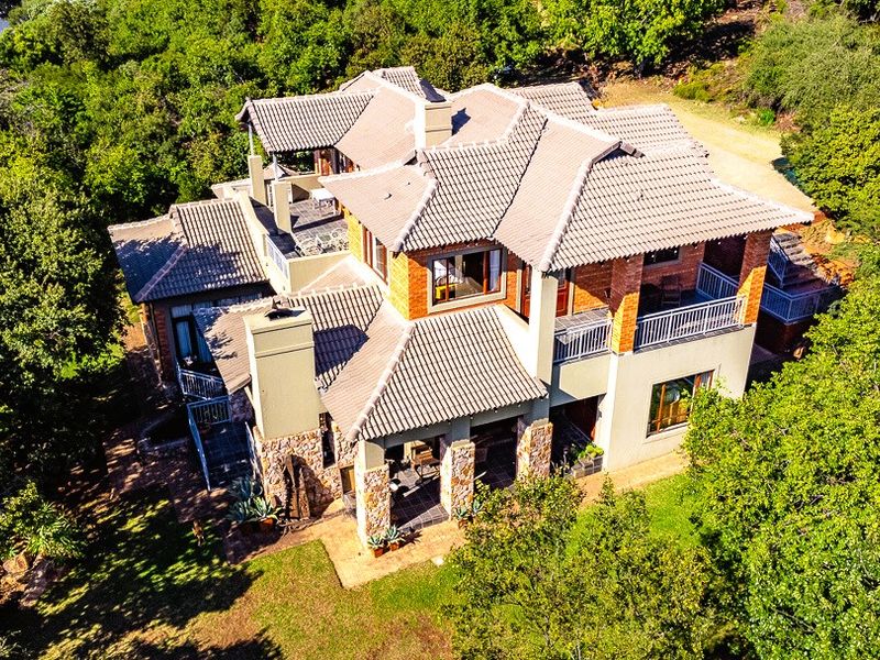 Aerial view of a multi-level residential property featuring a tiled roof, stone cladding, and multiple balconies set within a lush, wooded environment.
