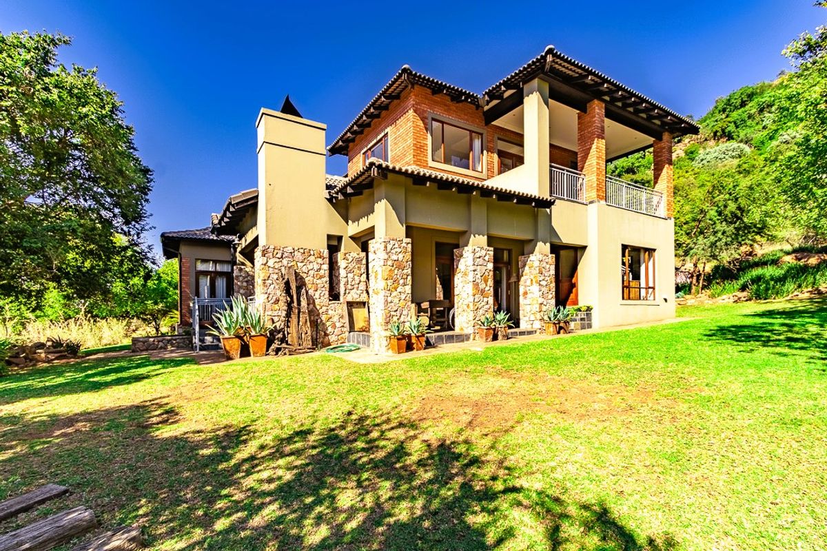 Rear view of a multi-story residence featuring stone and brick exterior finishes, a covered patio, and an upper-level balcony overlooking a landscaped garden.