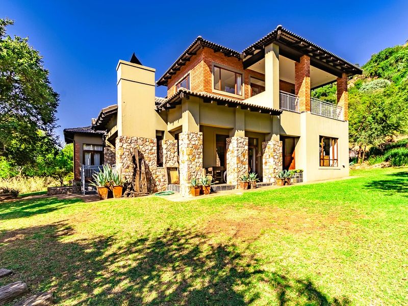 Rear view of a multi-story residence featuring stone and brick exterior finishes, a covered patio, and an upper-level balcony overlooking a landscaped garden.