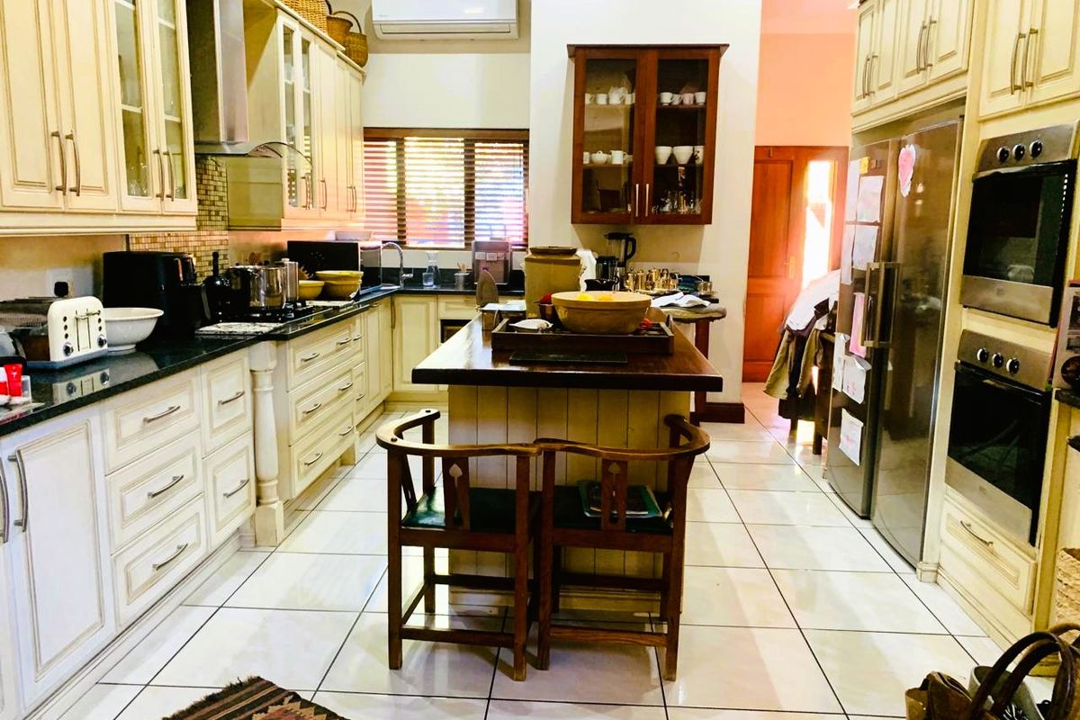Spacious kitchen featuring classic cream cabinetry, a central island, granite countertops, and integrated double wall ovens with tiled flooring throughout.