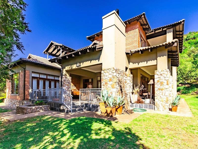 Rear view of a multi-level house featuring stone and brick exterior finishes, a covered patio area, and a well-maintained garden.