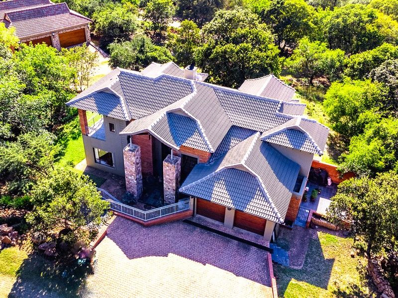 Aerial view of a large residential property featuring a tiled roof, stone-clad pillars, a spacious brick driveway, and a double garage set in a garden.
