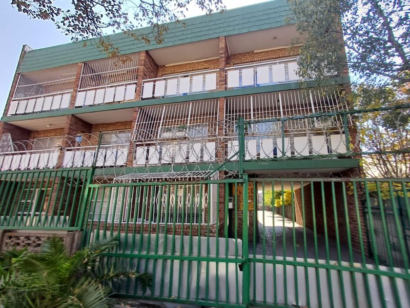 Front elevation of a multi-story brick apartment building featuring security fencing, razor wire, and private balconies with security bars.