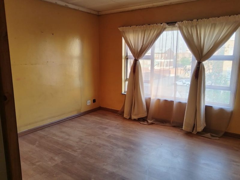 An empty bedroom featuring laminate flooring and a large window, requiring cosmetic updates to the walls and ceiling to improve its overall condition.