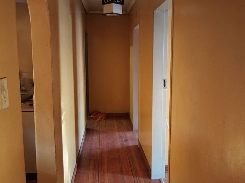 A narrow hallway featuring tiled flooring, an arched entryway, and a central ceiling light fixture, connecting multiple rooms within the flat.
