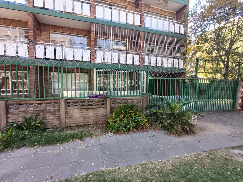 Front elevation of a multi-story brick apartment building featuring security fencing, razor wire, and balcony access.